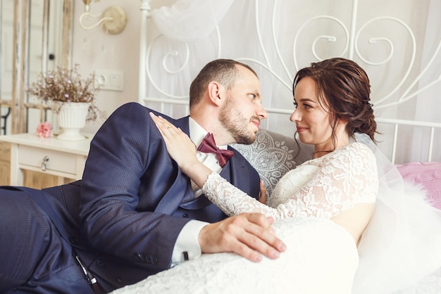 La giovane bella sposa della ragazza si siede su un letto con lo sposo in camera da letto