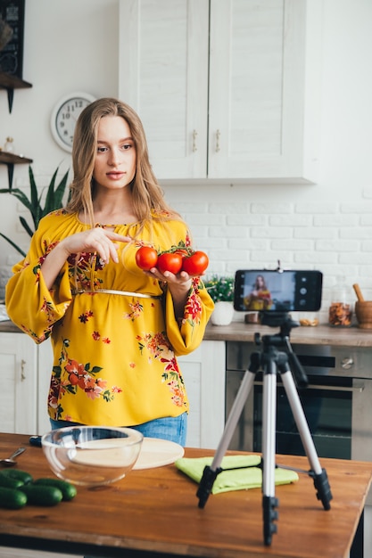 La giovane blogger di ragazza incinta abbastanza gira un video di una ricetta di insalata su una fotocamera dello smartphone