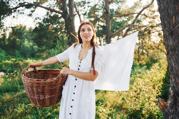 La giovane casalinga con il cestino in mano riattacca il panno bianco pulito lavato ad asciugare