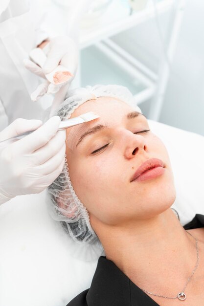 La giovane cliente del salone di cosmetica con una maschera per il viso pulente