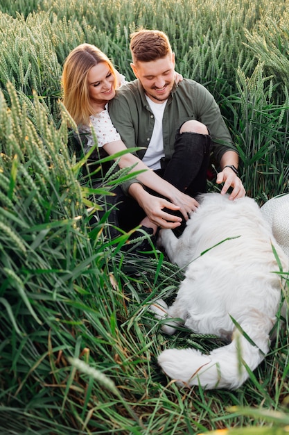 La giovane coppia accarezza il cane mentre cammina nei campi la sera d'estate. Amore e tenerezza. Bei momenti di vita. Giovinezza e bellezza. Pace e disattenzione. Camminare nella natura. Stile di vita.