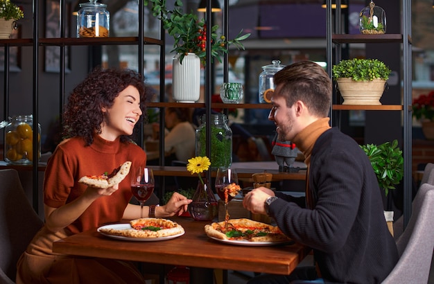 La giovane coppia adorabile sta mangiando la pizza in pizzeria. il ragazzo diverte la sua ragazza in un ristorante. Gente felice che si diverte insieme