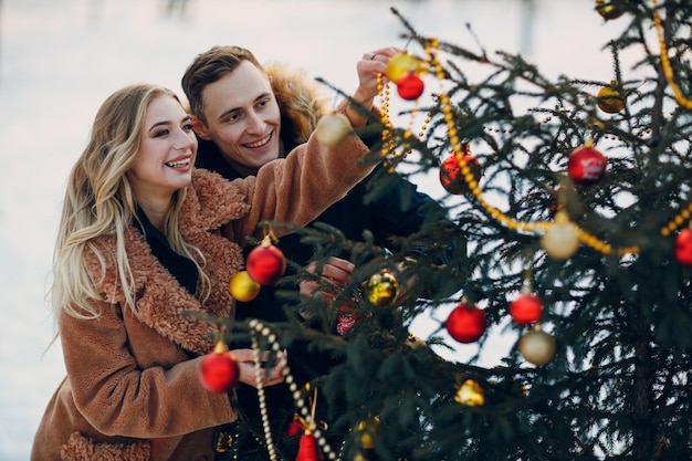 La giovane coppia adulta decora l'albero di Natale nella foresta invernale. Concetto di celebrazione del partito di festa del pino di Capodanno. addobbi per l'albero di natale