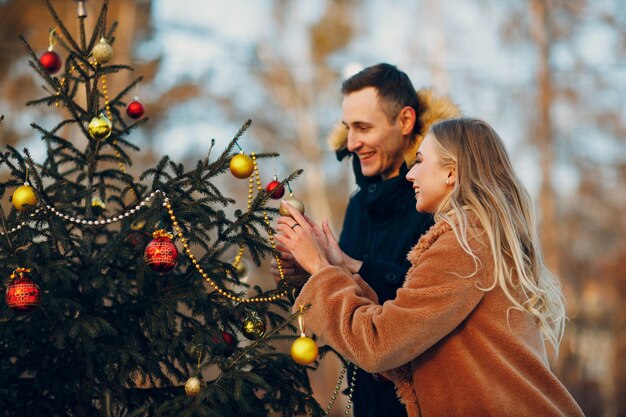 La giovane coppia adulta decora l'albero di Natale nella foresta invernale. Concetto di celebrazione del partito di festa del pino di Capodanno.