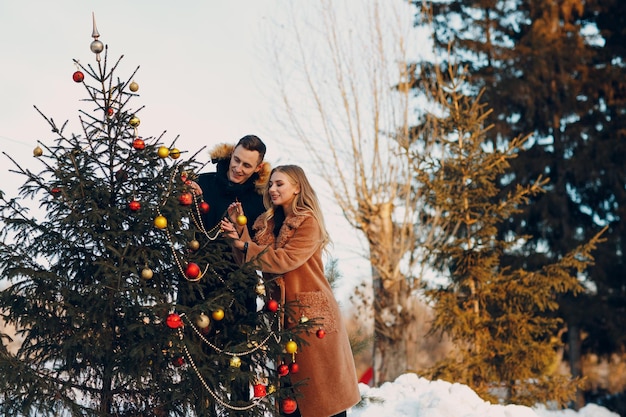 La giovane coppia adulta decora l'albero di Natale nella foresta invernale. Concetto di celebrazione del partito di festa del pino di Capodanno.