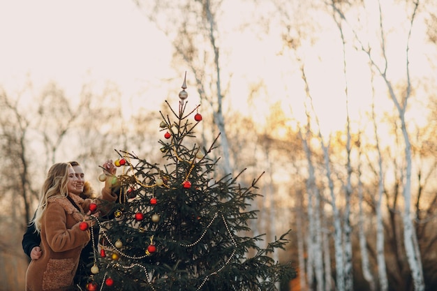 La giovane coppia adulta decora l'albero di Natale nella foresta invernale. Concetto di celebrazione del partito di festa del pino di Capodanno.