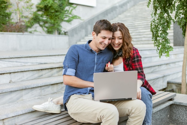 La giovane coppia allegra di amanti trascorre del tempo insieme mentre usa il laptop all'aperto. Persone felici e divertenti. Concetto di amore.