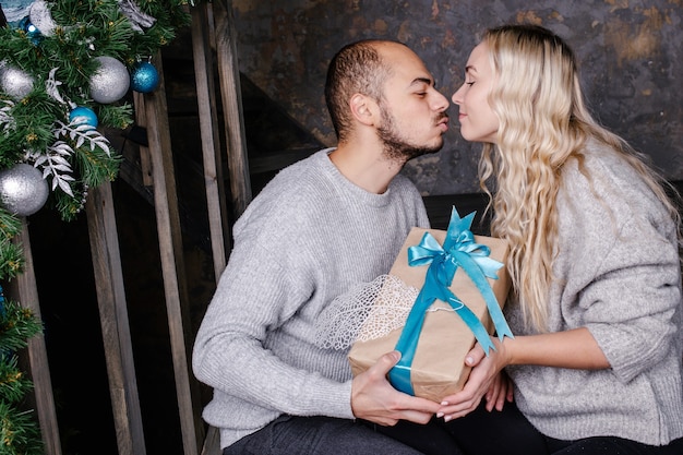 La giovane coppia amorosa scambia i regali per il nuovo anno. Il marito bacia la moglie e fa un regalo per il nuovo anno. Regalo di Natale e Capodanno a casa.