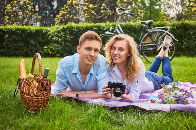 La giovane coppia attraente che utilizza una macchina fotografica compatta durante un picnic in un parco.