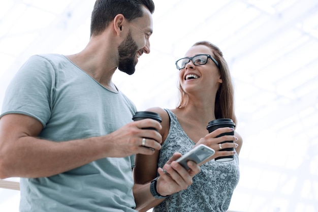 La giovane coppia beve il caffè e usa uno smartphone per strada o