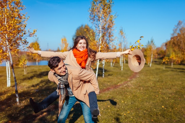 La giovane coppia cammina nella foresta di autunno. L'uomo dà la sua ragazza sulle spalle. Le persone si divertono