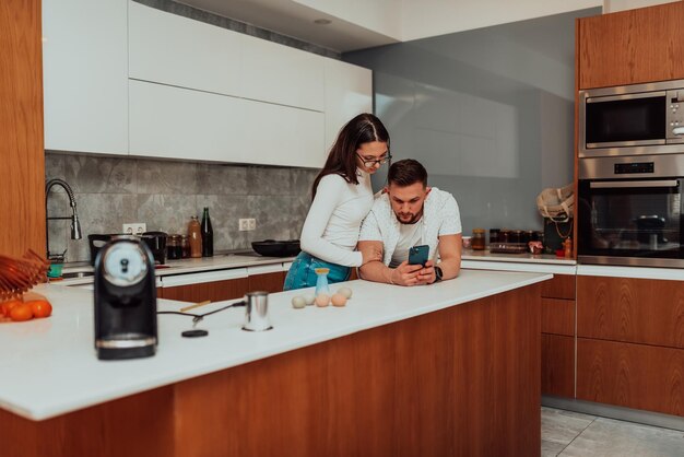 La giovane coppia felice che utilizza due telefoni condivide le notizie sui social media a casa sorridendo marito e moglie utenti millenari clienti che parlano facendo shopping online si siedono al tavolo concetto di stile di vita tech mobile