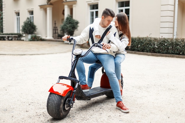 La giovane coppia felice in vestiti alla moda alla moda cavalca su una bici elettrica vicino all'hotel