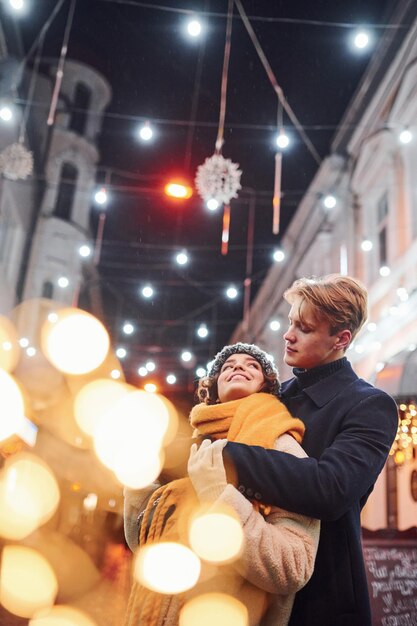 La giovane coppia felice in vestiti caldi è insieme sulla via decorata di natale.