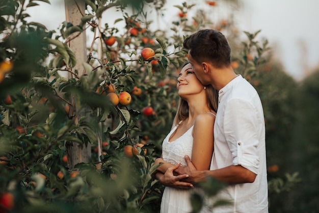 La giovane coppia felice sta abbracciando nel frutteto di autunno tra le mele rosse mature.