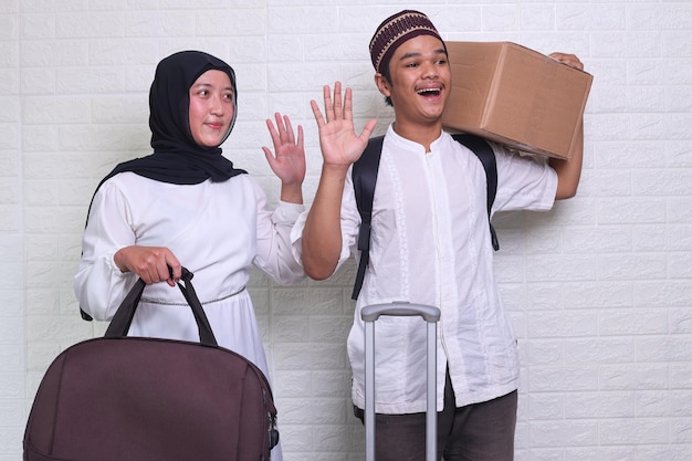 la giovane coppia musulmana porta bagagli e pacchi agitando le mani per viaggiare mudik al momento di eid mubarak