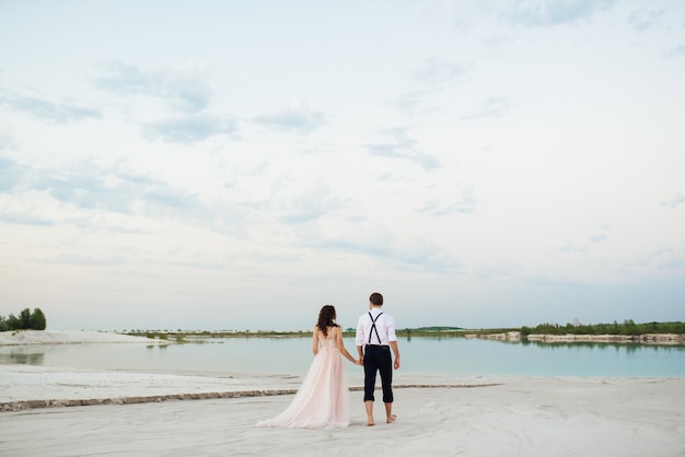 La giovane coppia un ragazzo in calzoni neri e una ragazza in un vestito rosa stanno camminando lungo la sabbia bianca del deserto