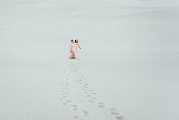 La giovane coppia un ragazzo in calzoni neri e una ragazza in un vestito rosa stanno camminando lungo la sabbia bianca del deserto