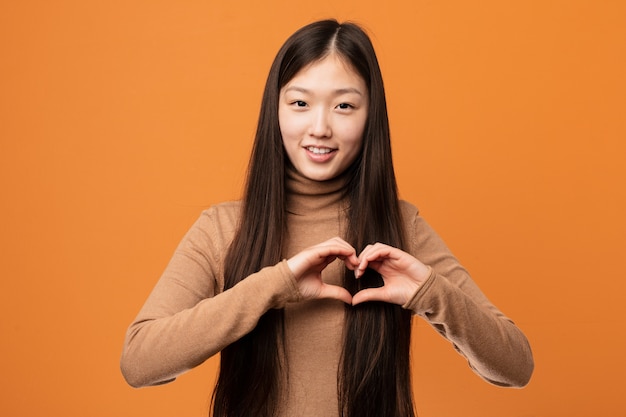 La giovane donna abbastanza cinese che sorride e che mostra un cuore modella con lui le mani.