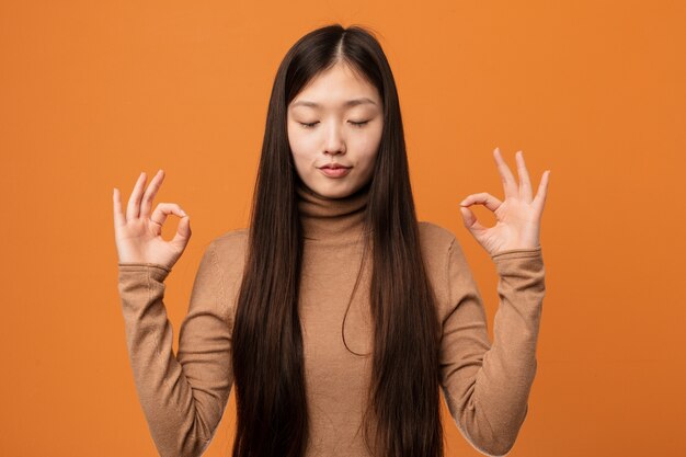 La giovane donna abbastanza cinese si rilassa dopo una dura giornata di lavoro, sta eseguendo yoga.