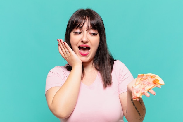 La giovane donna abbastanza formosa ha sorpreso l'espressione e tiene una pizza