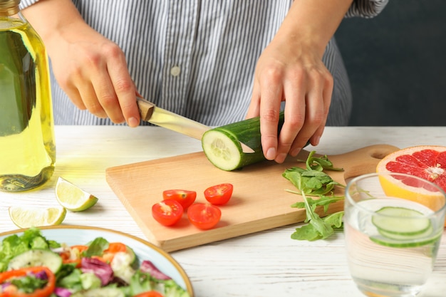 La giovane donna affetta il cetriolo per insalata su di legno