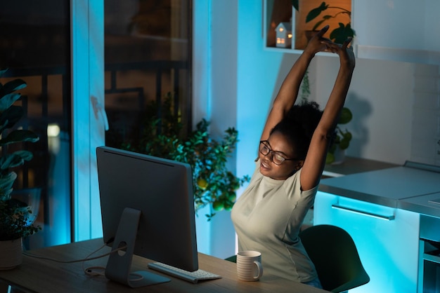 La giovane donna africana stanca si prende una pausa dal lavoro al computer a casa fa esercizio e stretching