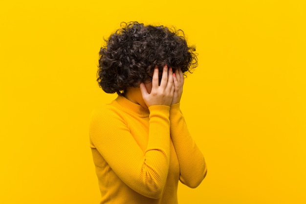 La giovane donna afro graziosa che copre gli occhi di mani con uno sguardo triste e frustrato di disperazione, piange, vista laterale