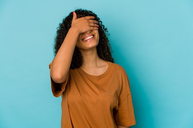 La giovane donna afroamericana afro isolata copre gli occhi con le mani, sorride ampiamente in attesa di una sorpresa.