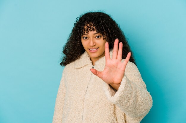 La giovane donna afroamericana afro isolata sorridente allegro che mostra il numero cinque con le dita.