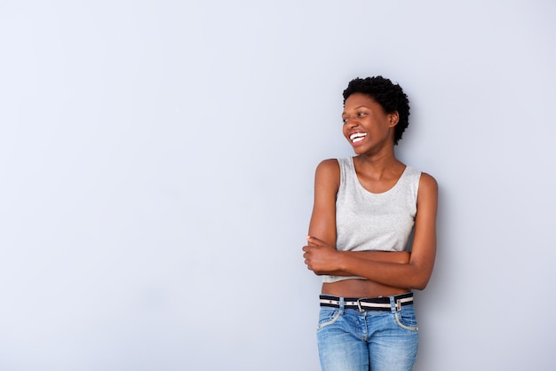 La giovane donna afroamericana allegra che ride con le armi ha attraversato dalla parete grigia