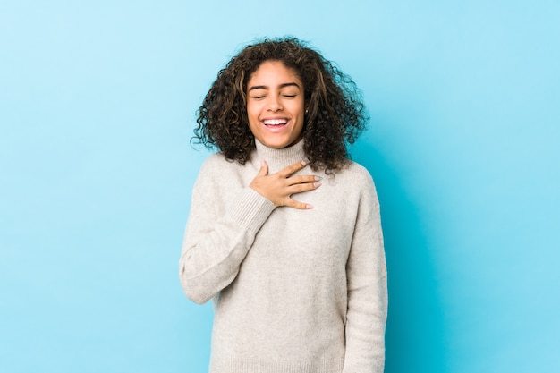 La giovane donna afroamericana capelli ricci ride ad alta voce mantenendo la mano sul petto.