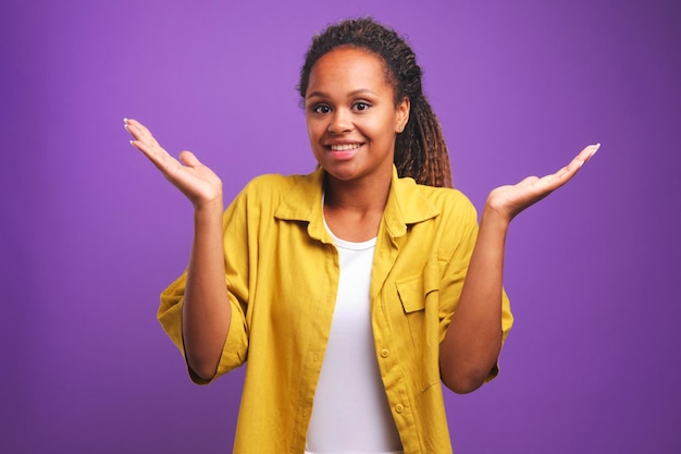 La giovane donna afroamericana che dubita che sorride alza le spalle e alza i palmi delle mani