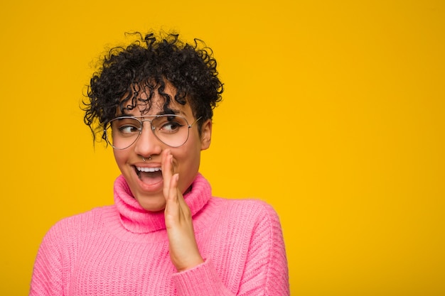 La giovane donna afroamericana che indossa un maglione rosa sta dicendo un segreto e sta guardando da parte