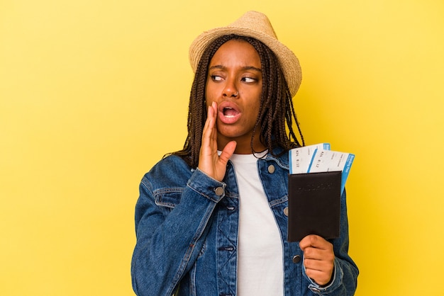 La giovane donna afroamericana che tiene il passaporto isolato su sfondo giallo sta dicendo una notizia segreta di frenata calda e sta guardando da parte