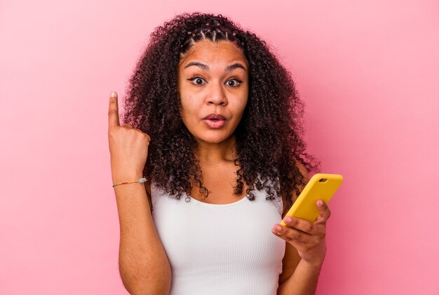 La giovane donna afroamericana che tiene un telefono cellulare ha isolato uno sfondo rosa con una grande idea, il concetto di creatività.