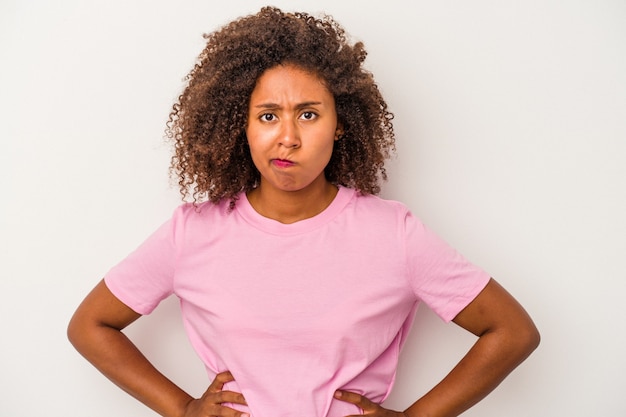 La giovane donna afroamericana con capelli ricci isolati su fondo bianco confuso, si sente dubbiosa e insicura.