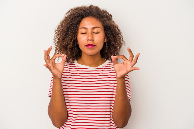 La giovane donna afroamericana con capelli ricci isolati su fondo bianco si rilassa dopo una dura giornata di lavoro, sta eseguendo yoga.