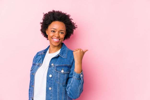 La giovane donna afroamericana contro un backgroound rosa ha isolato i punti con il dito del pollice via, ridendo e spensierato.