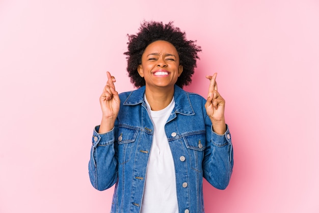 La giovane donna afroamericana contro un backgroound rosa ha isolato le dita dell'incrocio per avere fortuna