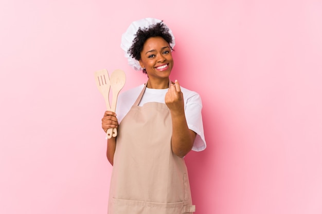 La giovane donna afroamericana del cuoco che indica con il dito contro di voi come se invitasse avvicinarsi.