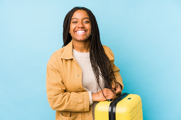 La giovane donna afroamericana del viaggiatore che tiene una valigia ha isolato la risata e divertiresi.