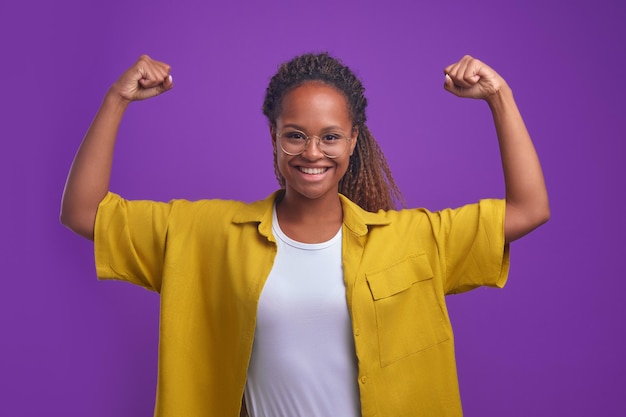 La giovane donna afroamericana felice forte che mostra i bicipiti sta in studio