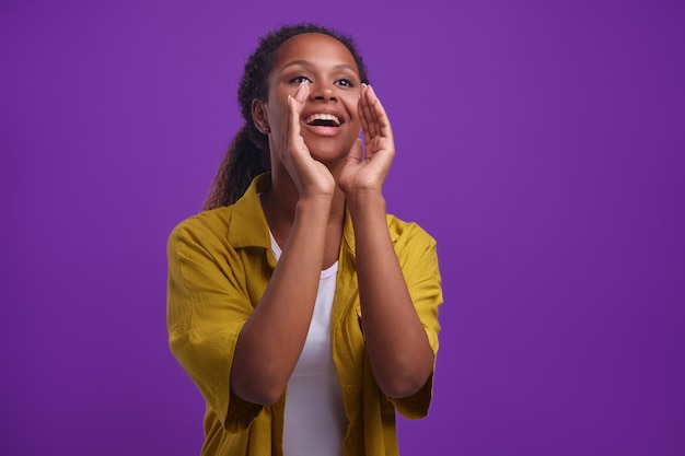 La giovane donna afroamericana felice mette le mani in bocca per gridare stand in studio