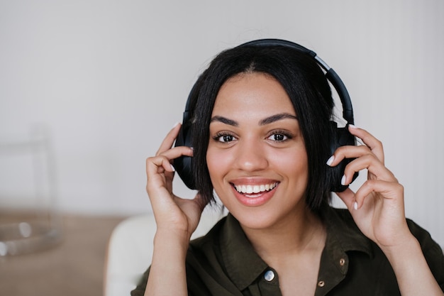 La giovane donna afroamericana in cuffia sorridente a trentadue denti tiene l'auricolare con un'espressione eccitata