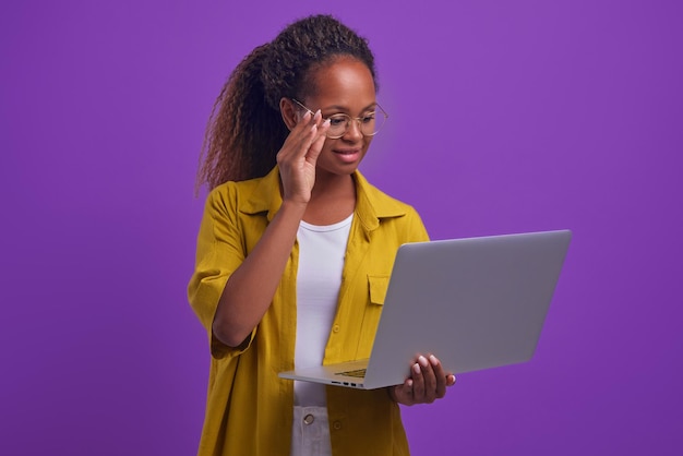 La giovane donna afroamericana intelligente tocca gli occhiali utilizza supporti per laptop in studio