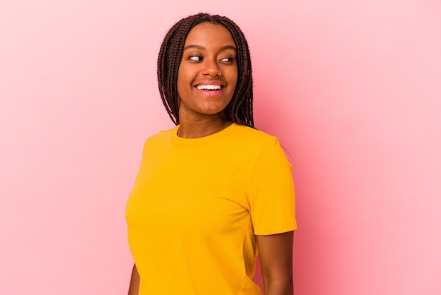 La giovane donna afroamericana isolata su fondo rosa guarda da parte sorridente, allegra e piacevole.