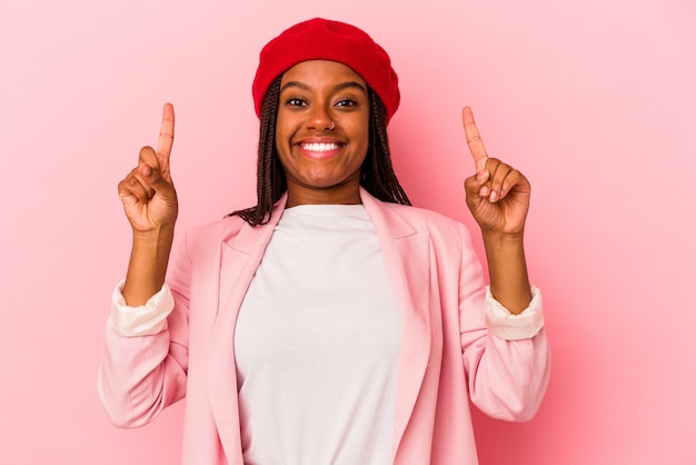 La giovane donna afroamericana isolata su fondo rosa indica con entrambe le dita anteriori in su mostrando uno spazio vuoto.