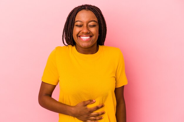 La giovane donna afroamericana isolata su fondo rosa tocca la pancia, sorride dolcemente, mangia e concetto di soddisfazione.