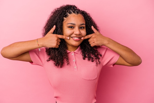 La giovane donna afroamericana isolata sui sorrisi rosa del fondo, indicando le dita alla bocca.